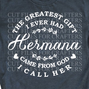 May include: A dark blue t-shirt with white text that reads "The Greatest Gift I Ever Had For Crafters Hermana Came From God I Call Her". The text is surrounded by a floral design.