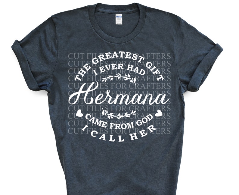 May include: A dark blue t-shirt with white text that reads "The Greatest Gift I Ever Had For Crafters Hermana Came From God I Call Her". The text is surrounded by a floral design.