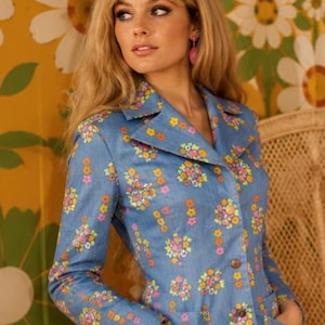 May include: A light blue blazer featuring a vibrant floral pattern with small yellow, pink, and orange flowers. The jacket has a collared neckline, long sleeves, two front pockets, and a button-down front closure with visible brown buttons.