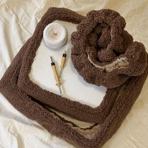 May include: A brown, fluffy, rectangular tote bag with a matching scrunchie and a ball of white yarn. Two wooden-handled tools are also present. The items are arranged on a white sheet, suggesting a craft or DIY project.