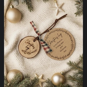 Puede incluir: Dos adornos navideños. Uno es una rodaja de madera con "Christmas hug" grabado. El otro es una etiqueta redonda con texto y un borde decorativo. Ambos están atados con una cinta a cuadros.
