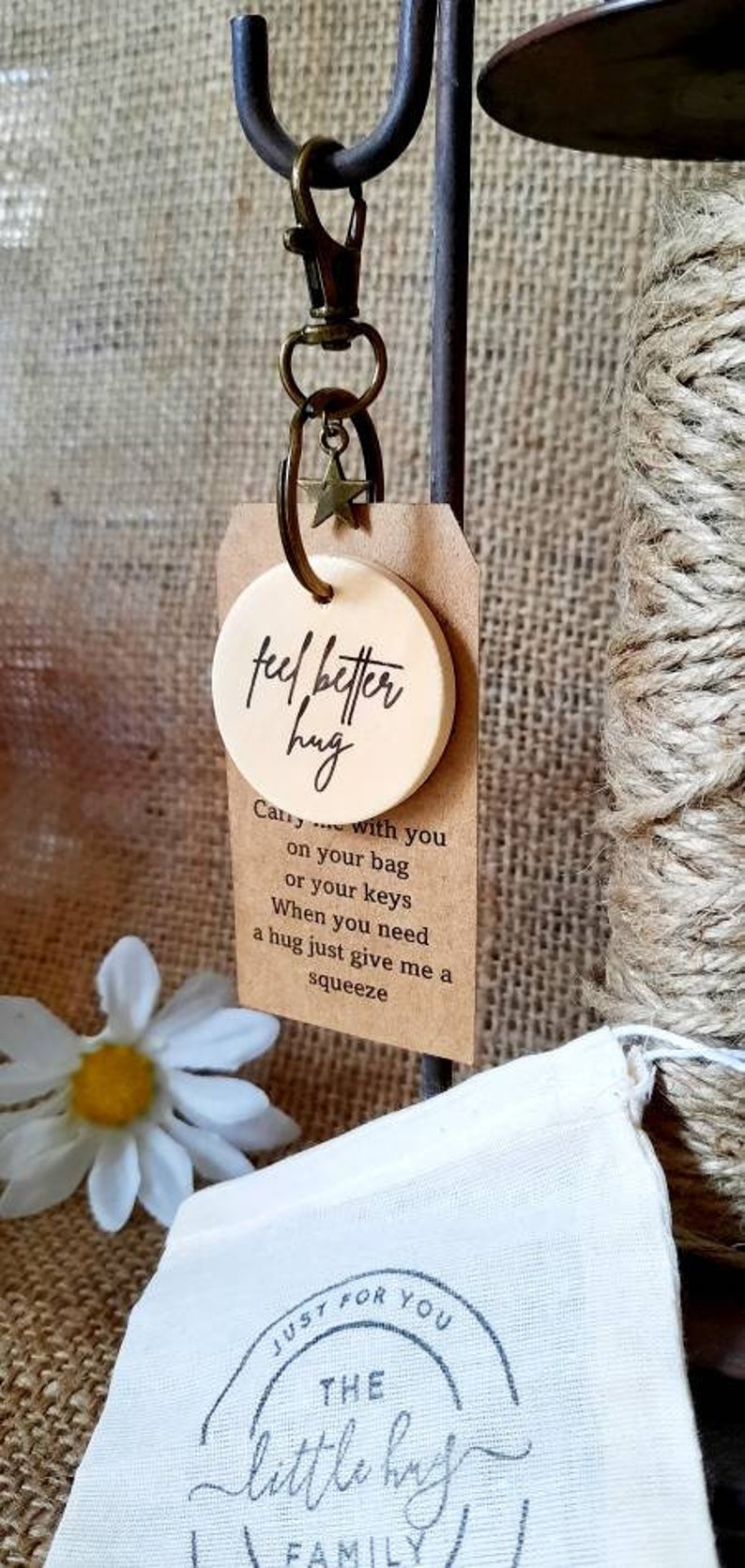 May include: A wooden keychain with a round tag that says "feel better hug". The tag is attached to a metal key ring with a star charm. The keychain is accompanied by a small fabric bag with the text "JUST FOR YOU THE little hug FAMILY" printed on it.
