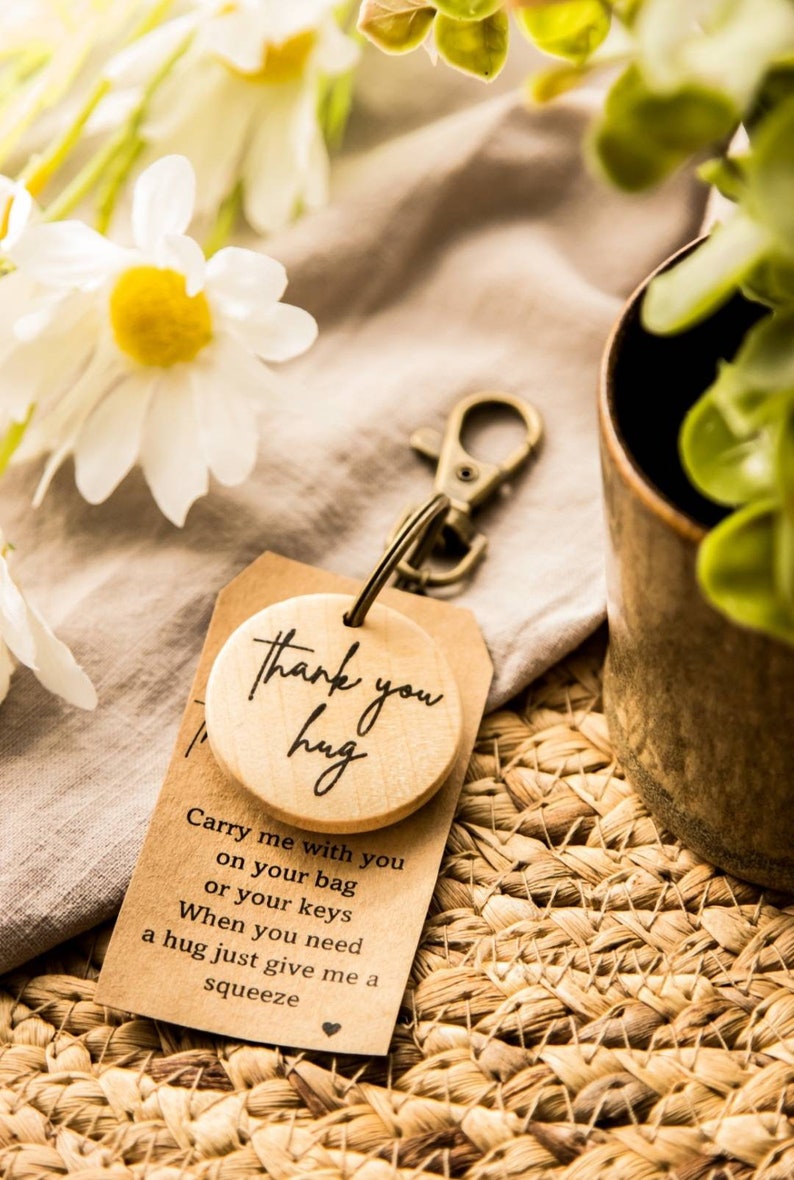 May include: A wooden keychain with a round wooden charm that says "Thank you hug". The charm is attached to a brown card with the text "Carry me with you on your bag or your keys. When you need a hug just give me a squeeze."