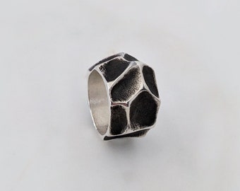 May include: A silver ring with a geometric, faceted design. The ring is textured and has a dark, almost black finish.