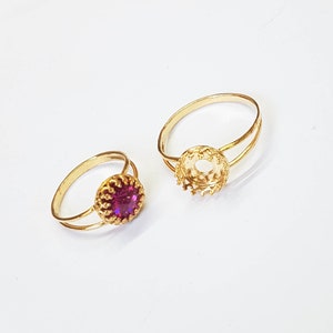 May include: Two gold rings with a bezel setting. One ring has a purple stone in the setting.