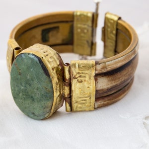 May include: A gold and brown bangle bracelet with a green stone set in a gold bezel. The bracelet has a hinged clasp.