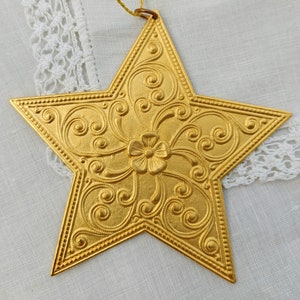 May include: A gold-coloured star-shaped ornament with an intricate floral design. The ornament has a loop at the top for hanging.