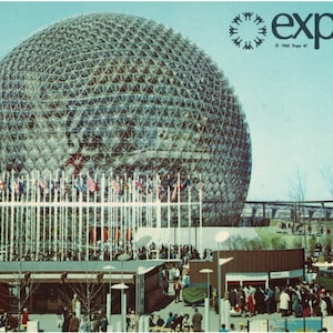 May include: A large, geodesic dome structure with a metal frame and glass panels. The dome is surrounded by a crowd of people and flags from different countries. The text "expo67" is visible in the top right corner of the image.