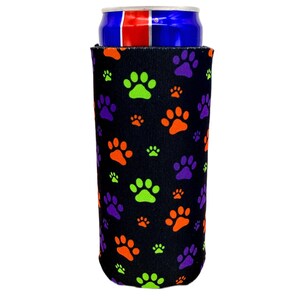 May include: Black beverage insulator featuring a pattern of colorful paw prints in green, orange, and purple. The insulator is designed to hold a standard-sized can and keep the beverage cold. The background is white.