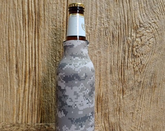May include: A gray and white camouflage beer bottle cooler. The cooler is made of neoprene and has a zipper closure.