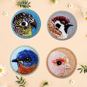 May include: Four round embroidered patches featuring bird portraits. The birds are depicted in vibrant colors, including blue, green, red, and pink, with detailed stitching. Each patch has a decorative border.