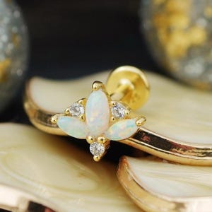 May include: A gold-toned flat back stud earring featuring a central marquise-cut white opal, flanked by two smaller marquise-cut opals and two round clear stones arranged in a symmetrical floral-inspired cluster design on a metal post.