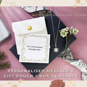 May include: A gold-colored necklace with a starburst pendant is displayed on a dark blue box, next to a white gift pouch and a card with the text "Your personalized message here." The image includes the text "NOTE CARD DESIGN MAY DIFFER" and "PERSONALISED MESSAGE & GIFT POUCH + BOX AVAILABLE."