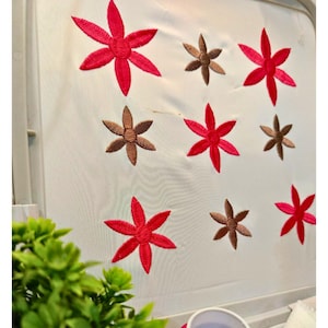 May include: Close-up of a white fabric with embroidered floral designs. The flowers are in shades of red and brown, arranged in a repeating pattern. The embroidery work is detailed and the colors are vibrant.