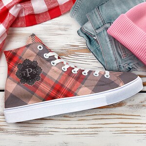 Peut inclure: Chaussures montantes en toile à motif écossais rouge et noir. Les chaussures ont des lacets blancs et une semelle blanche. Les chaussures ont un monogramme des lettres "TPS" dans un cercle noir avec une bordure décorative.