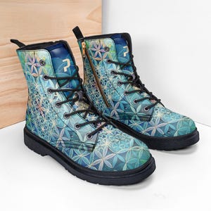 Puede incluir: Un par de botas hasta el tobillo con un patrón geométrico repetitivo de flores azules y turquesas. Las botas tienen cordones negros, suelas negras, una cremallera lateral y un logotipo con la letra P blanca en la lengüeta.