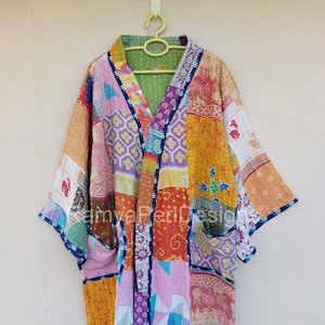 May include: A patchwork kimono-style robe with a variety of colorful fabric patterns. The robe features a green lining, pockets, and dark blue trim. It is hanging on a yellow hanger against a neutral background.