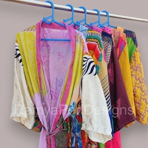 May include: A colorful patchwork kimono robe with a pink lining and a tie belt. The robe is made from a variety of fabrics, including silk and cotton. The robe is hanging on a clothes rack.