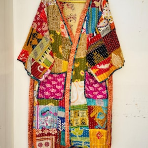May include: A patchwork kimono-style robe with a vibrant mix of colors and patterns. The robe features a variety of fabric squares in shades of red, blue, green, and yellow, with intricate designs. It has two front pockets and a tie closure.