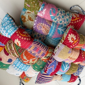 Peut inclure: Un coussin patchwork multicolore avec divers motifs de tissu. Le coussin est composé de plusieurs morceaux de tissu cousus ensemble, avec des motifs floraux, géométriques et abstraits dans des tons de rouge, bleu, vert et violet. Il a des liens en tissu.