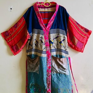 May include: A long-sleeved robe featuring a patchwork design with a dark blue upper section, a central panel with bird illustrations on branches, and a teal lower section. It has a bright pink floral trim, two front pockets, and a matching tie belt.