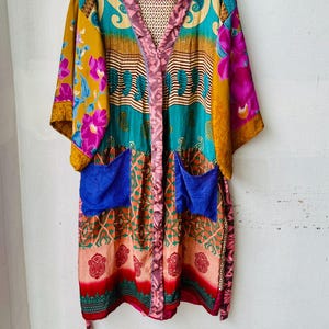 Può includere: Una vestaglia kimono lunga fino al ginocchio caratterizzata da un vivace patchwork di tessuti multicolori. Il capo presenta vari motivi tra cui disegni floreali, paisley e geometrici in tonalità ottanio, giallo senape, magenta e blu, con due tasche blu.