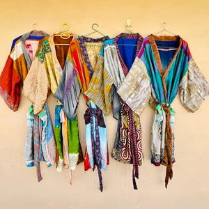May include: A collection of colorful, patterned robes hanging on a wall. The robes feature a variety of colors, including red, blue, green, and gold. Each robe has a unique design and is made of a lightweight fabric.