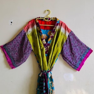 May include: A multi-colored kimono robe featuring a patchwork design with purple, lime green, and red fabric panels. The garment includes wide sleeves, a tie-waist belt, and a vibrant mix of floral and geometric patterns throughout the textile.