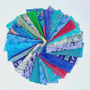 Può includere: Una collezione di ritagli di tessuto colorati in tonalità di blu, verde e rosa. Il tessuto è disposto in cerchio, con i bordi di ogni ritaglio che si sovrappongono. Il tessuto è decorato con vari disegni, tra cui floreali, geometrici e paisley.