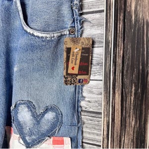 May include: Close-up of light blue denim shorts with a heart-shaped patch. A brown tag with the text "Handmade with Love" and social media icons is attached. The shorts have a distressed look.