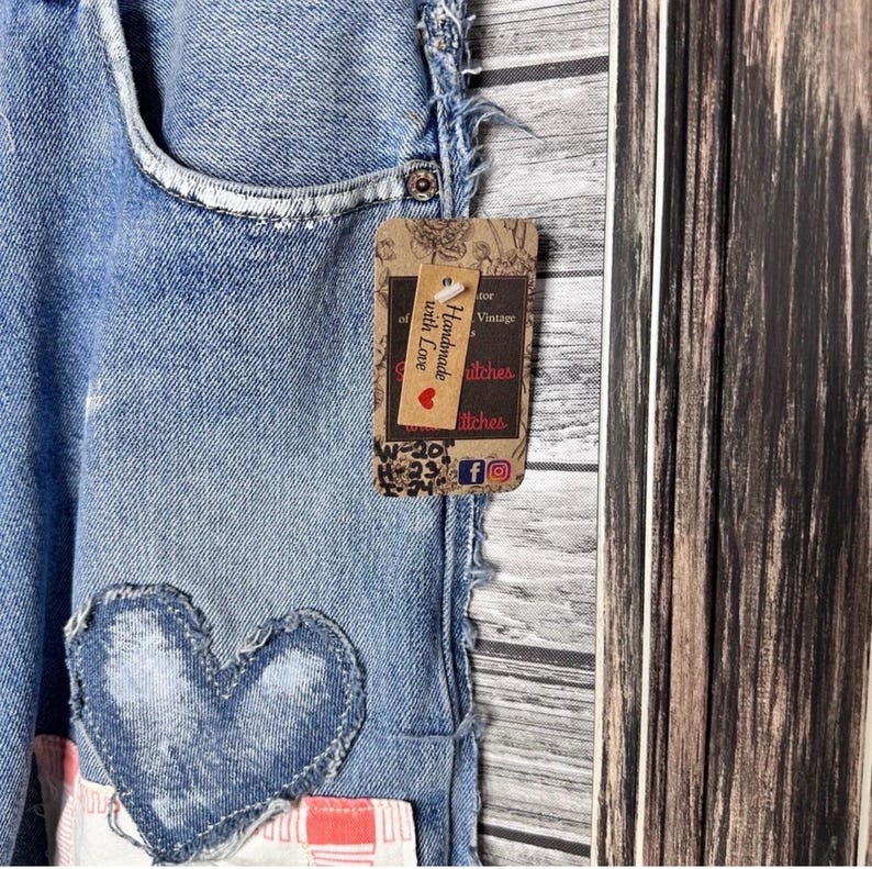 May include: Close-up of light blue denim shorts with a heart-shaped patch. A brown tag with the text "Handmade with Love" and social media icons is attached. The shorts have a distressed look.