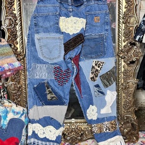 Puede incluir: Vaqueros azules con detalles de patchwork. Los parches incluyen encaje, estampado de leopardo y una tela en forma de coraz&oacute;n. Los vaqueros tienen un aspecto desgastado con bordes deshilachados y una etiqueta Carhartt.
