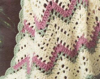 May include: A crocheted blanket featuring a chevron pattern in cream, dusty rose, and sage green. The textile has an openwork stitch design and a scalloped edge border in sage green, showcasing a soft, textured yarn construction throughout.