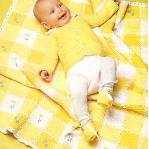 Può includere: Una copertina per neonato in crochet giallo con un bordo in crochet bianco e fiori ricamati. Un bambino è sdraiato sulla copertina indossando un cardigan in crochet giallo e pantaloni bianchi.