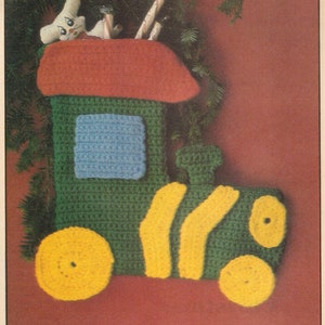 May include: A green and yellow crocheted train stocking with a red and green roof. The stocking has a blue window and a white crocheted mouse peeking out of the roof. The text "Hang a Train Stocking on the Mantle" is printed below the stocking.
