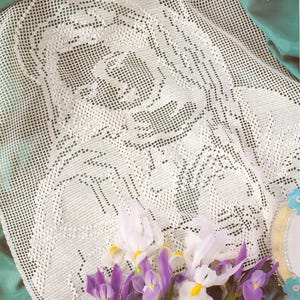 Puede incluir: Un mantel de encaje blanco tejido a ganchillo con un diseño floral. El mantel está drapeado sobre una superficie verde y está decorado con un ramo de iris blancos y morados. Un espejo decorativo está en el fondo.