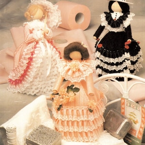 Peut inclure: Trois cache-rouleaux de papier toilette en forme de poupées faites à la main. Une poupée porte une robe rose avec une garniture en dentelle blanche et tient un parasol. Une autre poupée porte une robe noire avec une garniture en dentelle blanche et un chapeau blanc.
