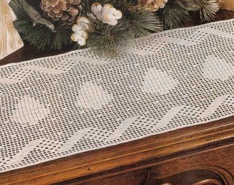 May include: White crocheted table runner with a scalloped edge and a repeating pattern of diamond shapes. The runner is on a wooden table.