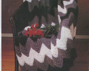 May include: A gray and white chevron crochet throw blanket draped over a black wicker chair. The blanket is made with a simple stitch pattern and has a soft, cozy texture.