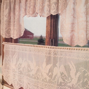 May include: A pair of crocheted valances with a delicate floral pattern. The valances are made of white thread and have a scalloped edge. The valances are hung on a window with a view of a red barn and green trees.