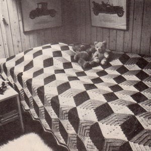 May include: A bed covered with a geometric patterned quilt in shades of black, white, and gray. Two teddy bears sit on the bed. The room has wood-paneled walls and framed vintage car prints.