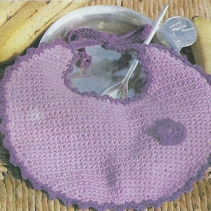 May include: A handmade crochet baby bib in shades of lavender and purple. The bib features a scalloped edge and a small decorative flower. The bib is designed to be tied around the neck.