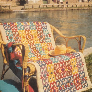 May include: A wicker chair with a colorful woven throw blanket and a straw hat on top. The blanket has a geometric pattern in shades of red, yellow, blue, green, and purple.