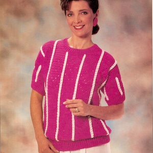 May include: A magenta short-sleeved sweater with vertical white stripes. The sweater has a crew neck and ribbed cuffs and hem. The woman in the image is wearing a white skirt and pink earrings.