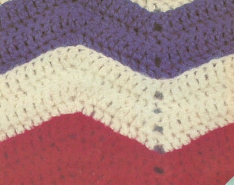 May include: Close-up of a crocheted blanket with a chevron pattern in red, white, and purple.
