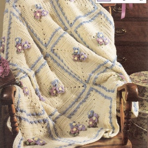 May include: A crocheted throw blanket with a delicate floral design in shades of purple, blue, and green. The blanket is draped over a wooden rocking chair. The text "Touch of Spring" is visible in the upper right corner of the image.