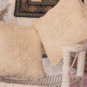 Puede incluir: Dos almohadas de crochet de color crema con un diseño floral en una silla de mimbre blanca.
