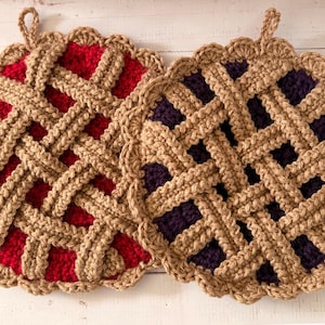 Può includere: Due presine all'uncinetto fatte a mano a forma di torta. Uno ha un ripieno rosso, l'altro un ripieno viola scuro. Entrambi hanno una crosta a griglia marrone e bordi smerlati. Ogni presina ha un piccolo anello per appenderla.