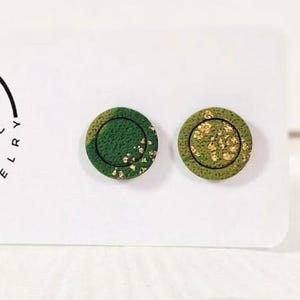 Op de afbeelding: Een paar ronde oorknopjes met een getextureerd bosgroen oppervlak en ingebedde bladgoudvlokken. De oorbellen worden gepresenteerd op een witte rechthoekige kaart met de zwarte tekst Petruša Unique Jewelry.