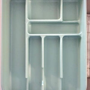 May include: A light blue plastic utensil organizer with multiple compartments. The rectangular tray has a large section on the left and several smaller, divided sections on the right, designed for organizing silverware and kitchen tools.